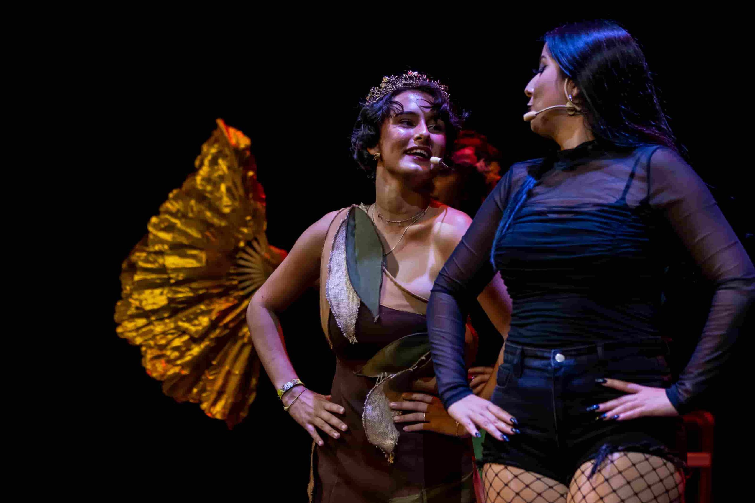 Primer plano de dos actrices interactuando en el escenario con iluminación cálida.