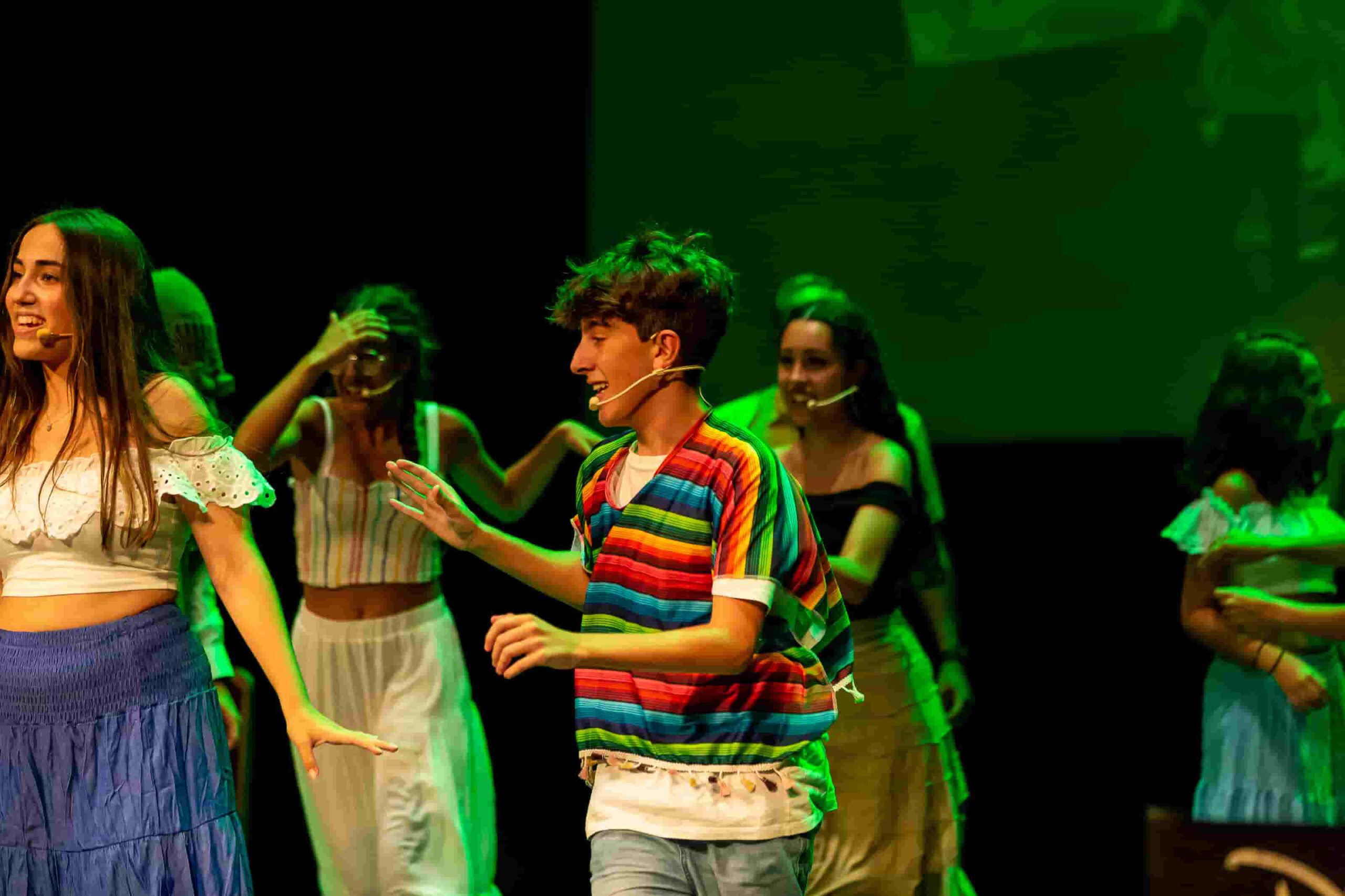 Actor joven con camiseta de rayas coloridas bailando en una coreografía grupal.