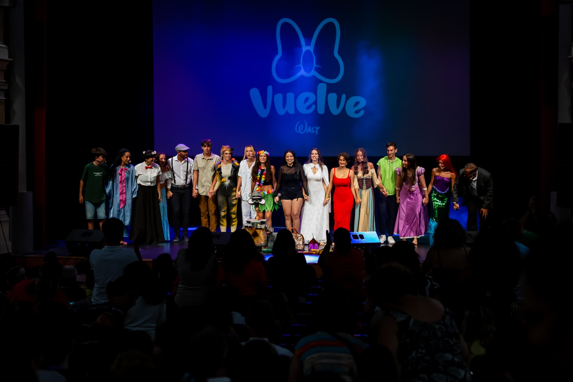 Elenco completo saludando al final del musical "Vuelve" con logo al fondo.